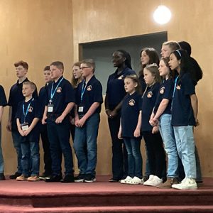 Young people in blue shirts singing on a stage.