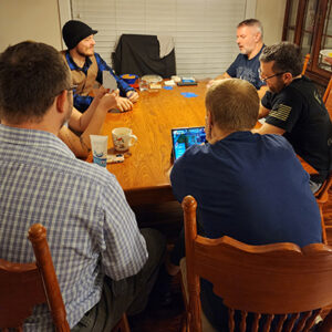 People around a dining table talking with snacks and a laptop.